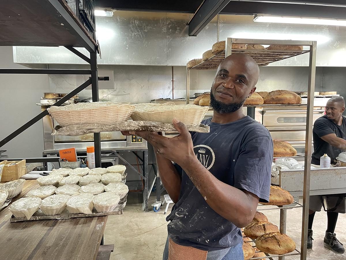 A baker carrying a tray of proving baskets past the ovens